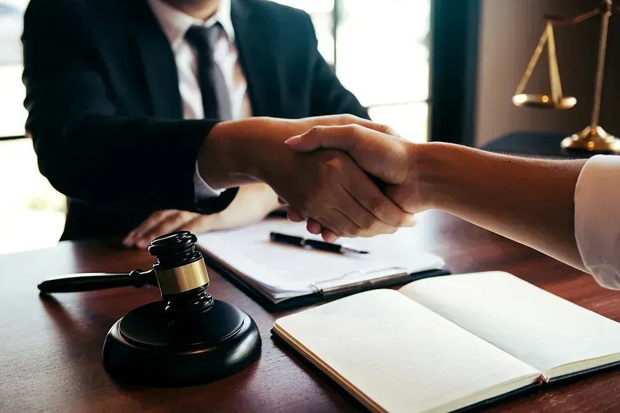 Un abogado le estrecha la mano a un cliente mientras está sentado en un escritorio.