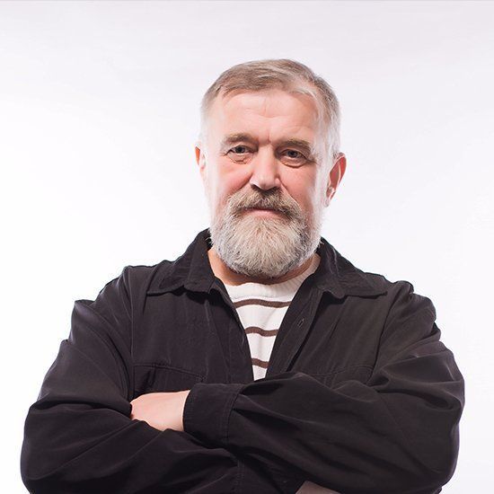 Un hombre con barba está de pie con los brazos cruzados.