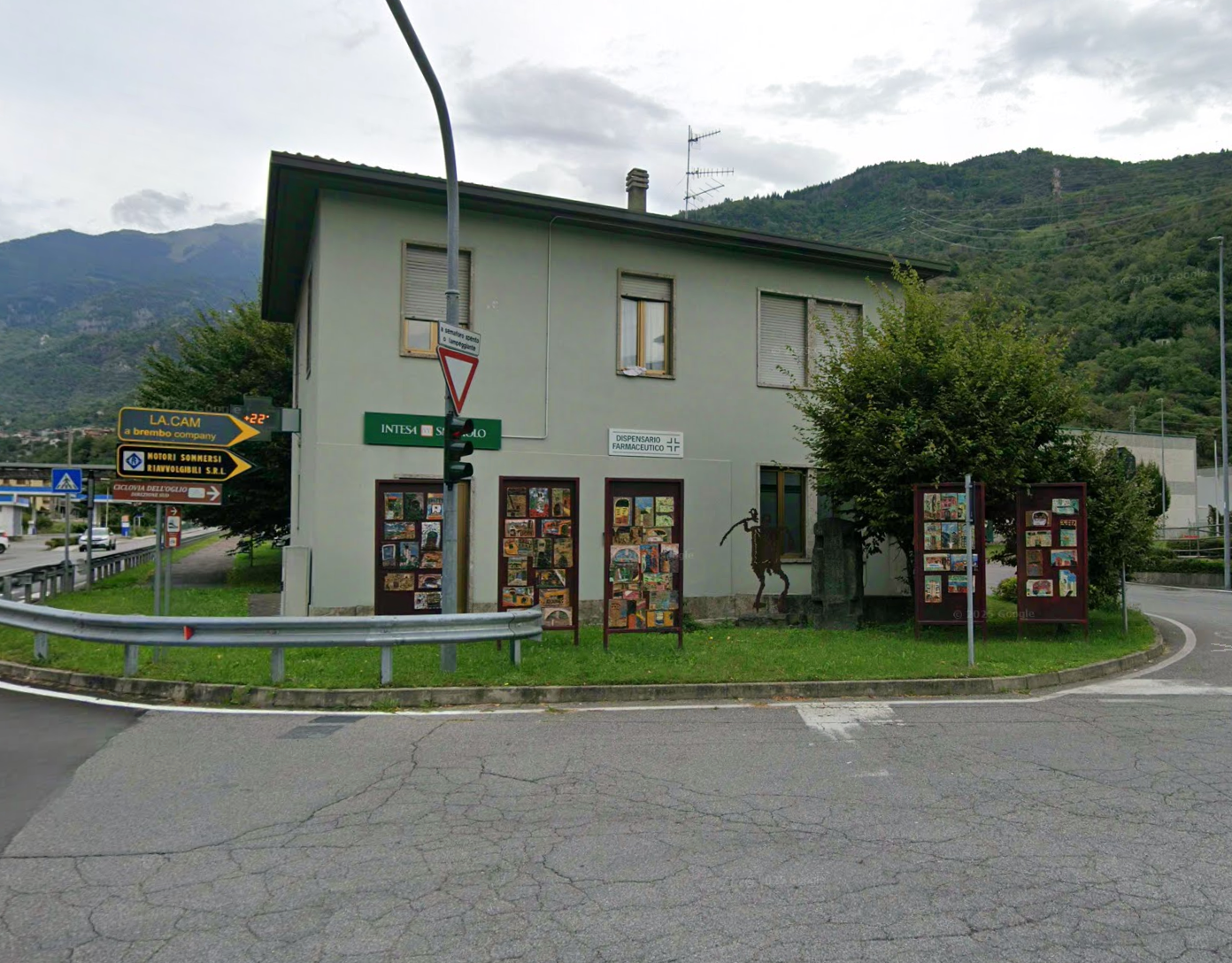 Farmacista in camice bianco sorride, braccia incrociate, in una farmacia con scaffali pieni di medicinali.