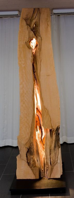 Eine grosse Holzskulptur, aus der Licht austritt, steht auf einem Tisch in einem Raum.