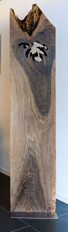 Auf einem gefliesten Boden neben einer Wand liegt ein grosses Stück Holz.