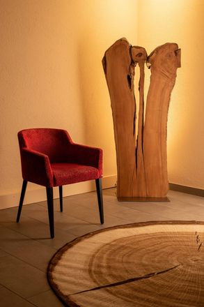 In einem Raum steht ein roter Stuhl neben einer Holzskulptur.