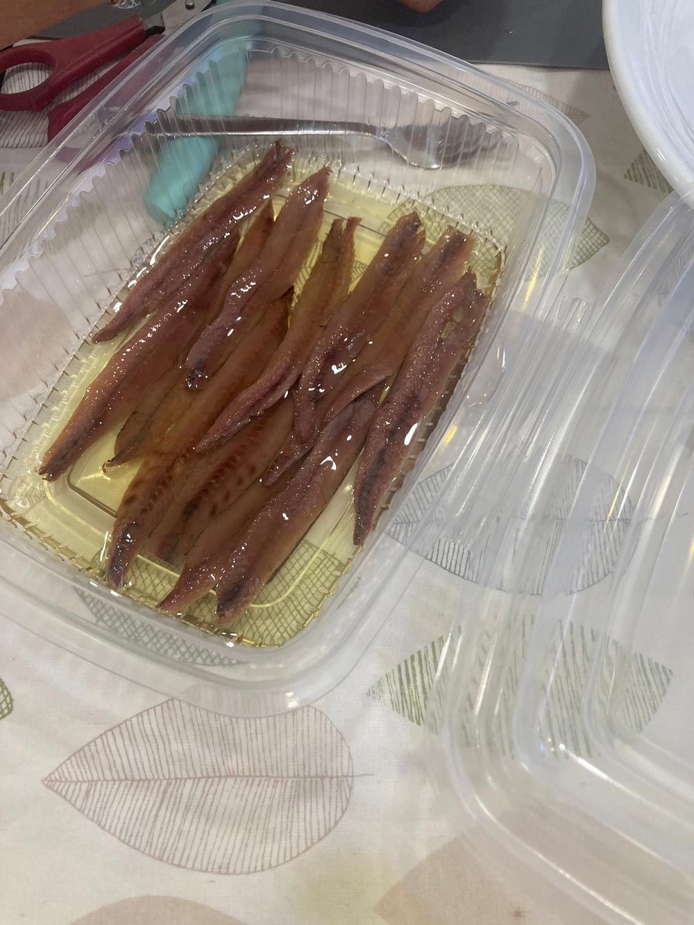 Un recipiente de plástico lleno de anchoas está sobre una mesa.