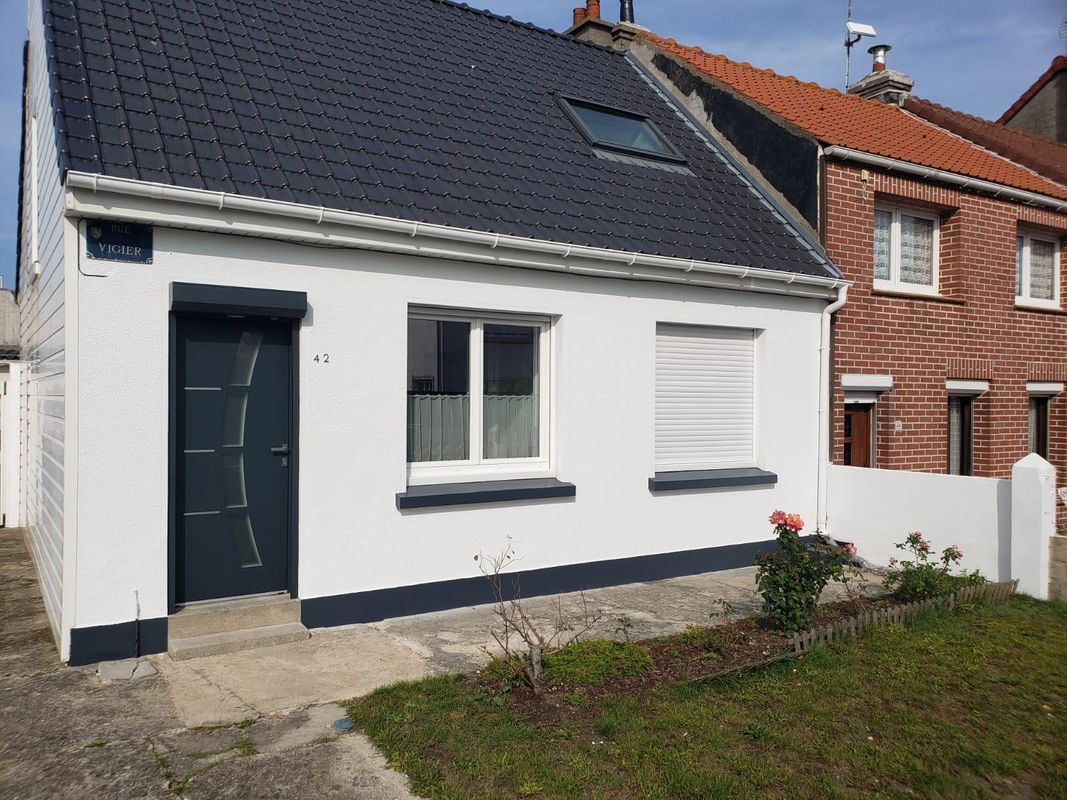 Maison blanche au toit et à la porte noirs. À droite, une fenêtre aux stores fermés.