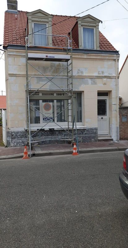 Un bâtiment de deux étages en rénovation, avec échafaudages, fenêtres et toit en tuiles rouges.