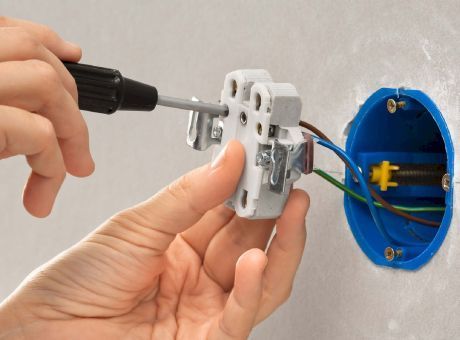 Una persona está arreglando un interruptor de luz con un destornillador.