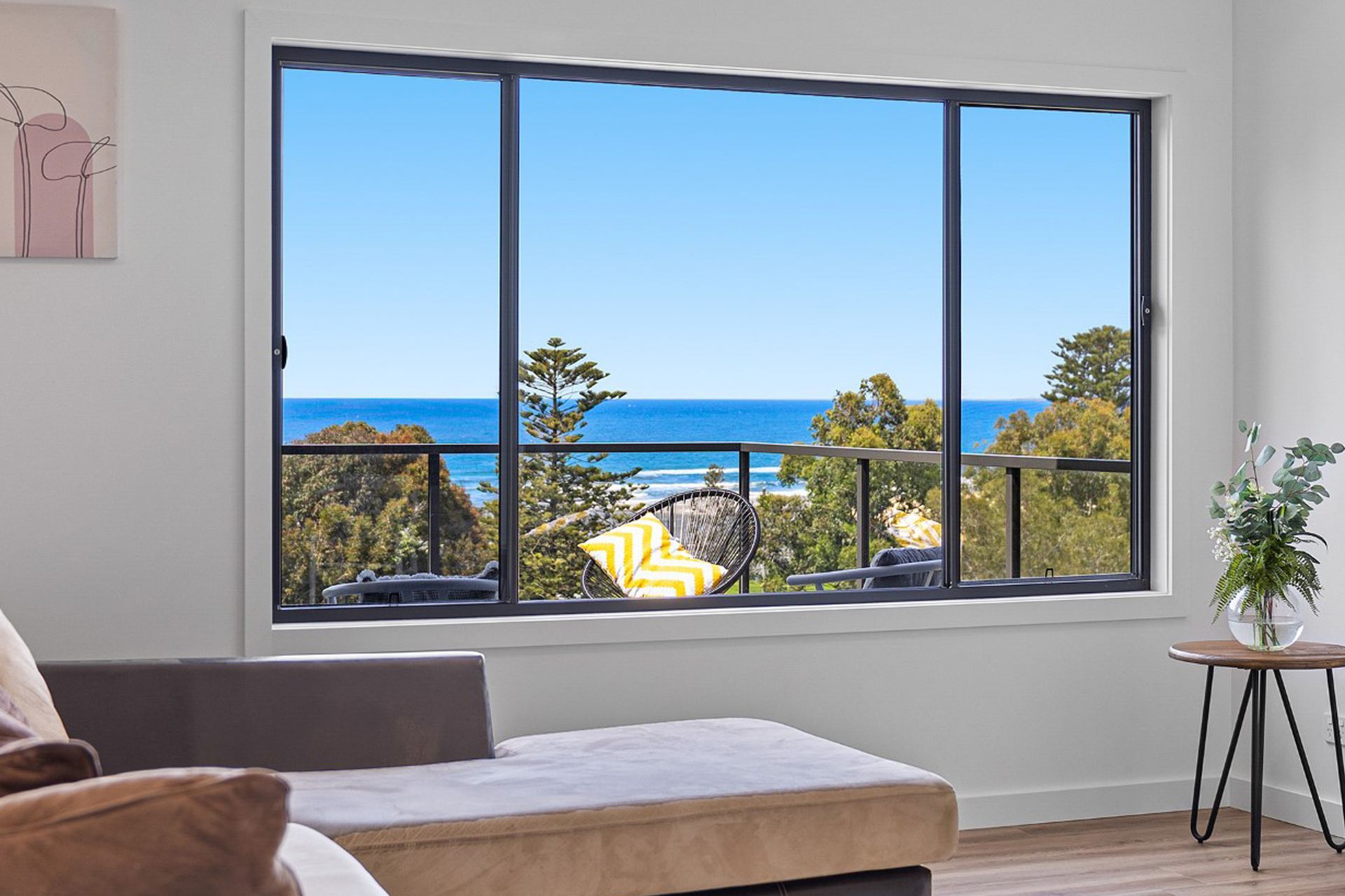 Living room with large window overlooking ocean and trees, bright blue sky outside