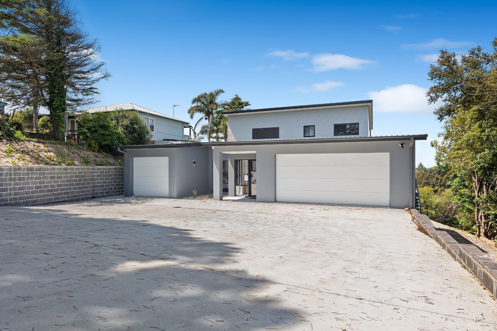 Modern gray house with garage, gravel driveway, and trees under a blue sky