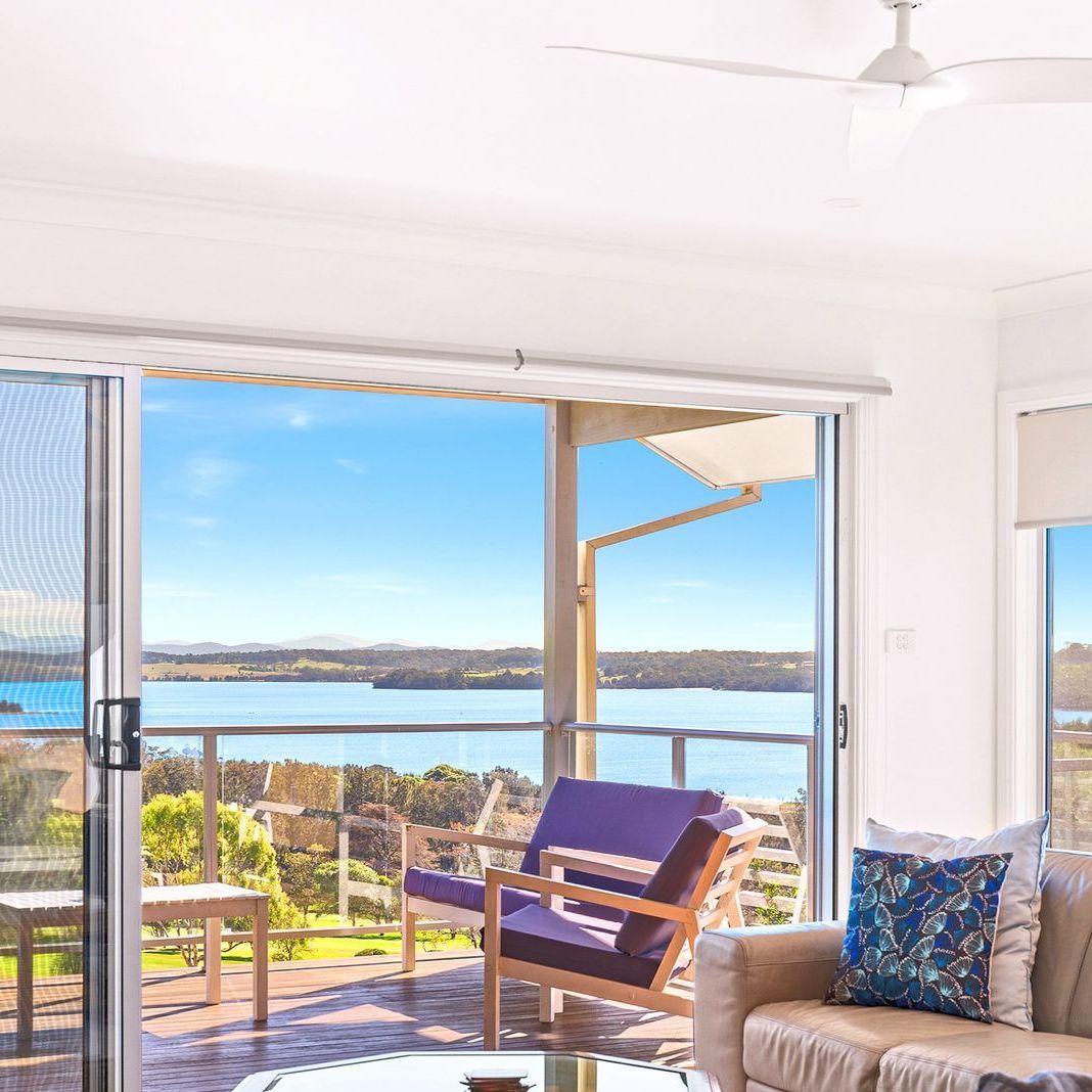 Living room with sliding door open to a sunny waterfront view, chair, and sofa.