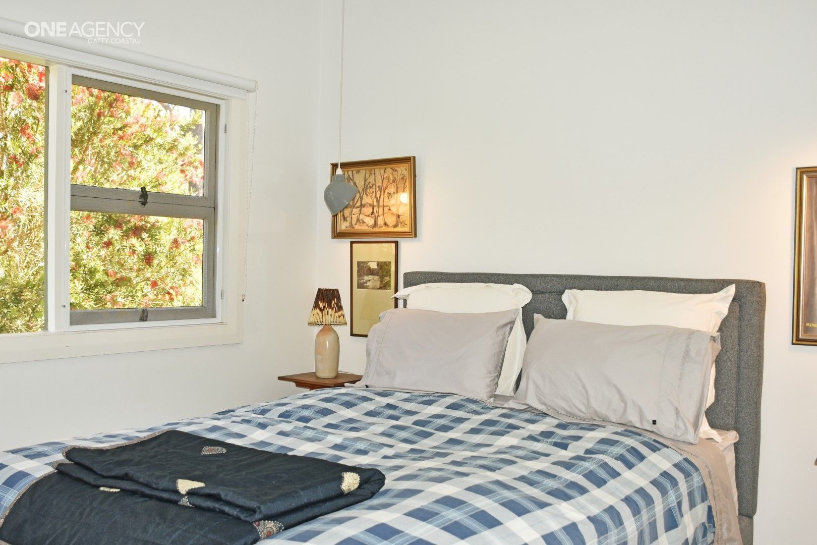 Bedroom with a bed, window, and small side table. Blue and white plaid bedding with grey pillows.