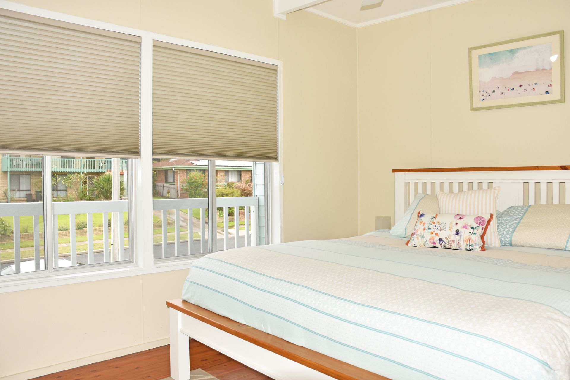 Bedroom with a bed, two windows with blinds, and a framed art piece.