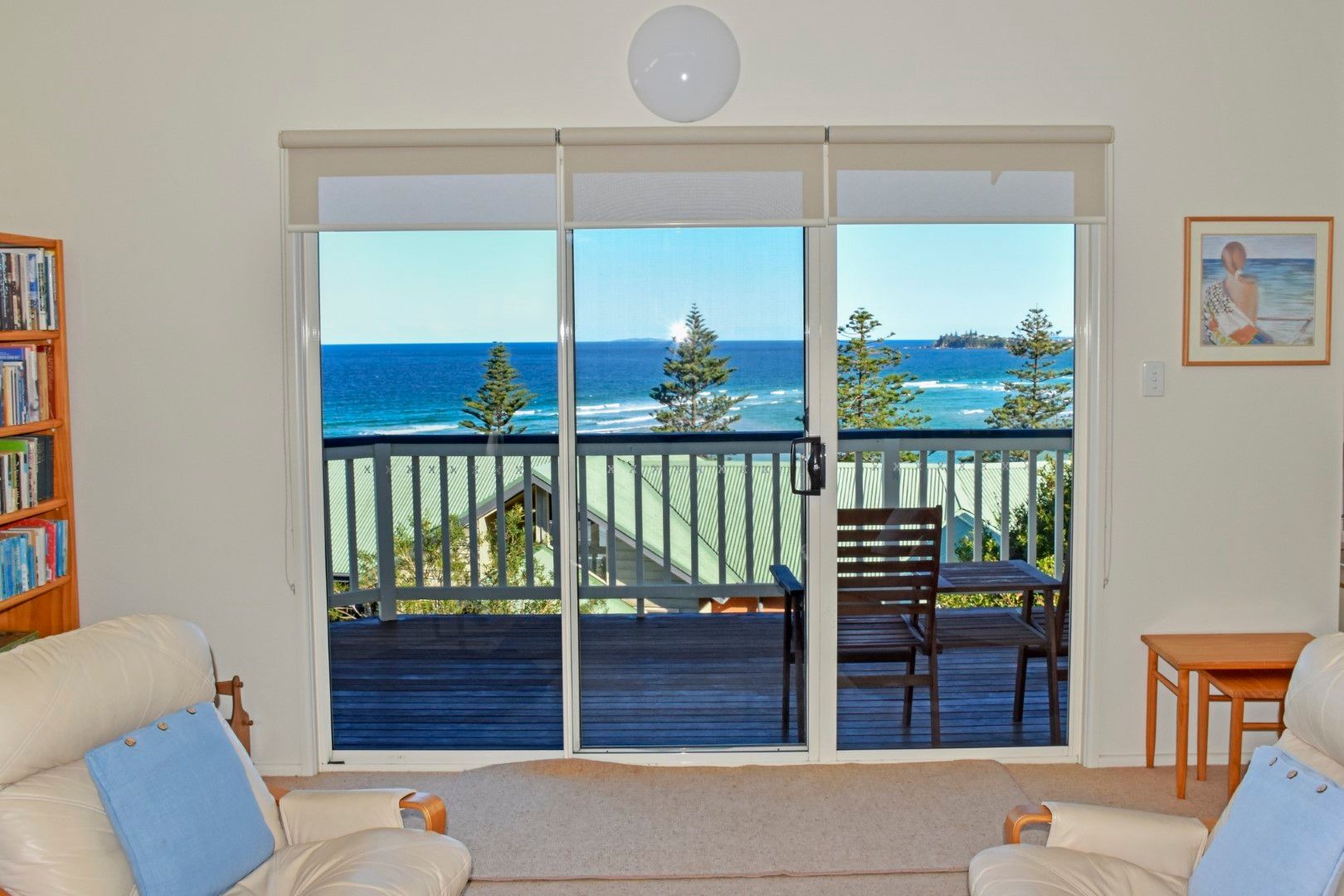 Living room with sliding glass doors opening to a ocean-view deck and blue sea beyond
