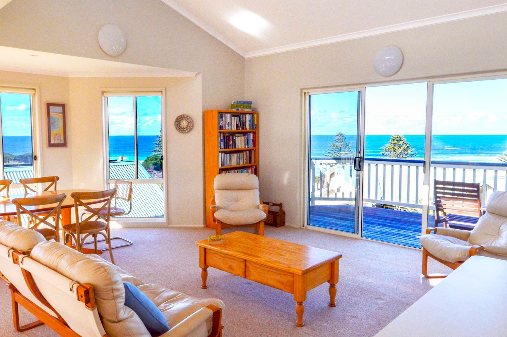 Bright living room with ocean view, sliding glass doors, wicker chairs, and a wooden coffee table