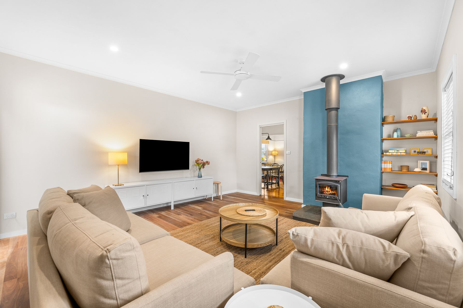 Bright modern living room with beige sofas, wall-mounted TV, blue fireplace, and woven rug