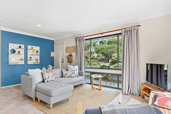 Bright living room with blue accent wall, gray sectional, large window, and plants outside.