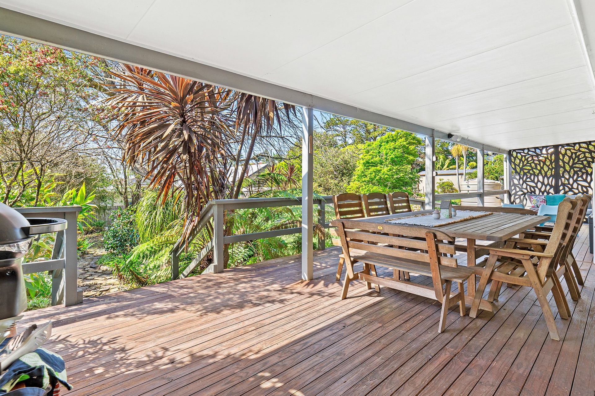 Covered wooden deck with outdoor dining table and chairs, overlooking a leafy garden