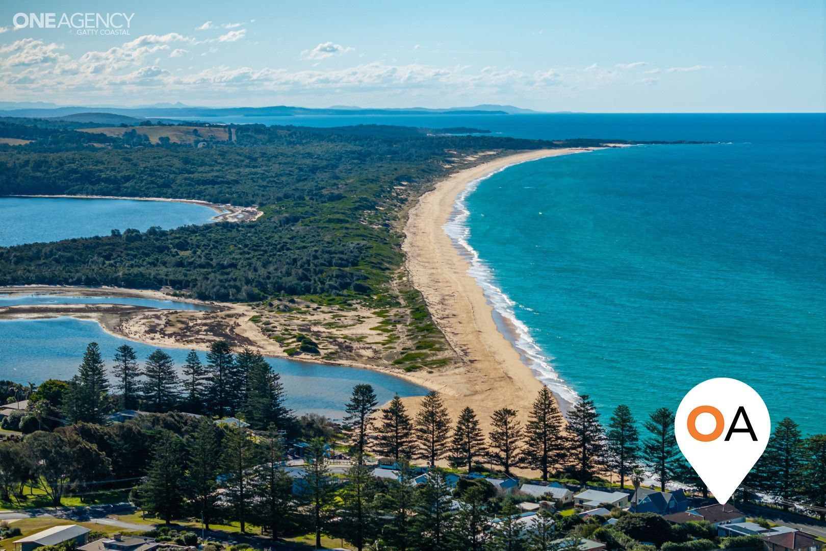 Aerial view of a sandy beach curving along a blue ocean beside a forested coastline