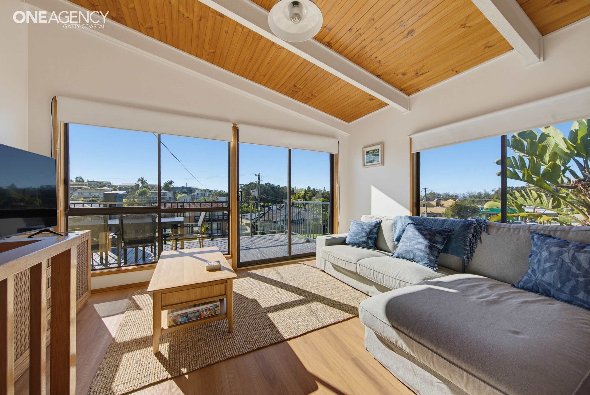 Sunlit upstairs living room with timber ceiling and balcony at The Waves, a family holiday home in Tuross Head.