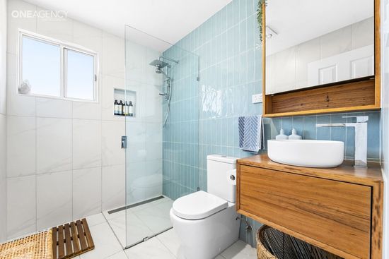Whale Watcher @ Tuross Head - Modern white bathroom with glass shower, toilet, wood vanity, and blue tile accent wall