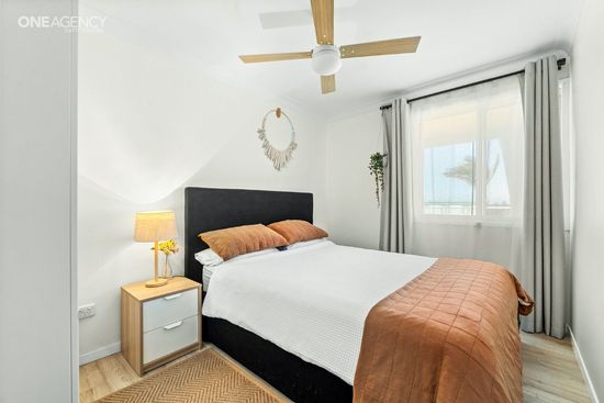 Whale Watcher @ Tuross Head - Bright bedroom with a black bed, white bedding, tan throw, bedside lamp, and large window 