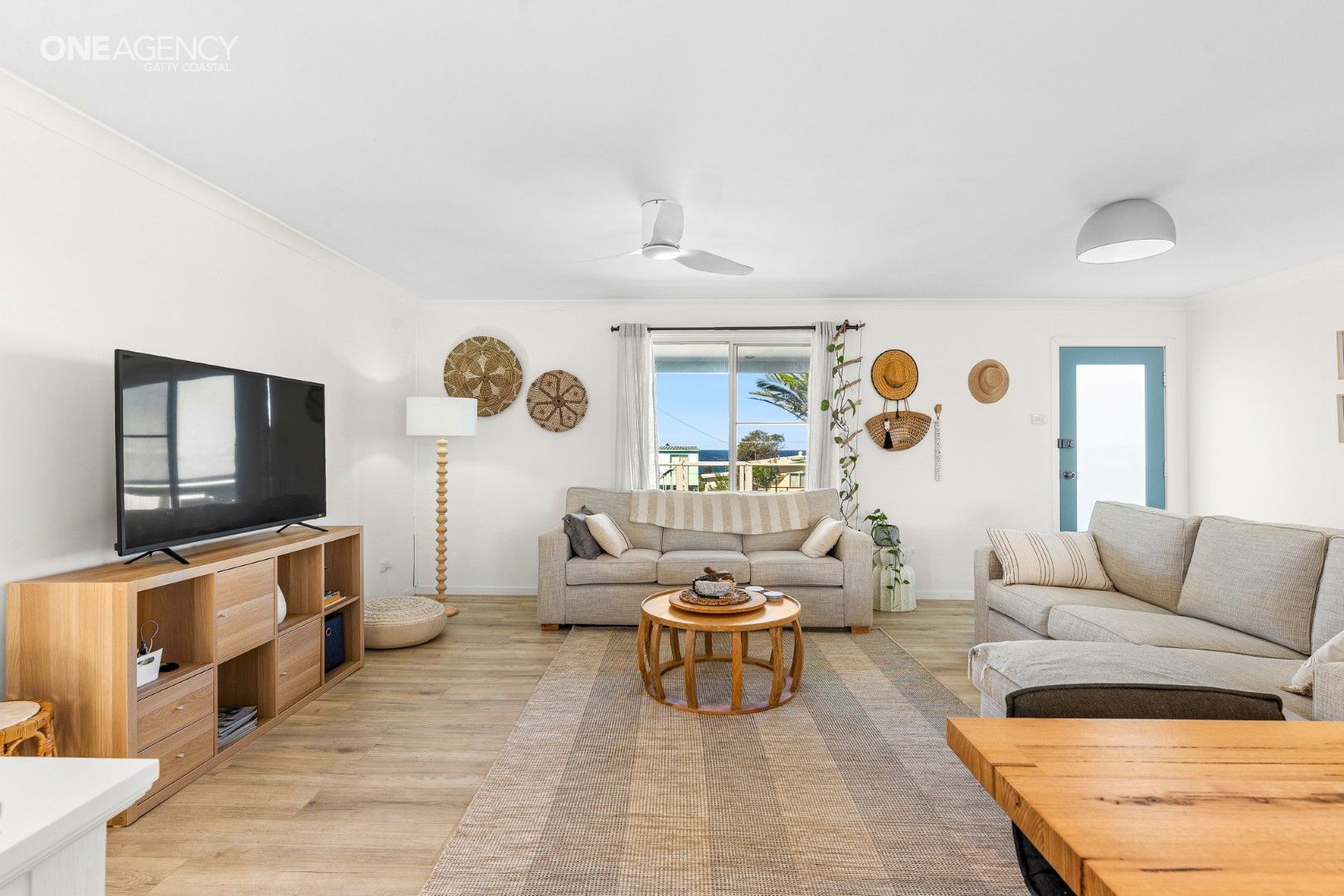 Bright living room with beige sofas, wood coffee table, TV, and ocean view through a window.