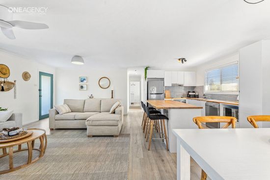 Whale Watcher @ Tuross Head - Bright open-plan living room and kitchen with beige sofa, wood floors, and white dining table.