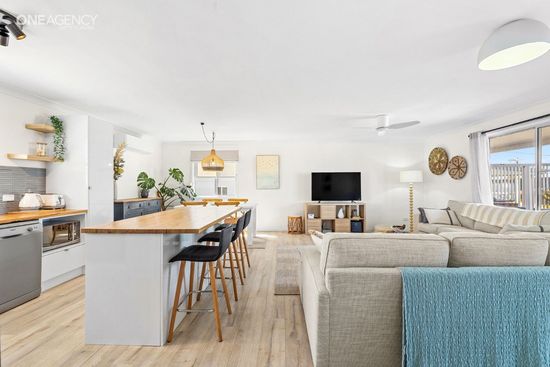 Whale Watcher @ Tuross Head - Bright open-plan living room with beige sectional, blue chair, kitchen island,  wall-mounted TV