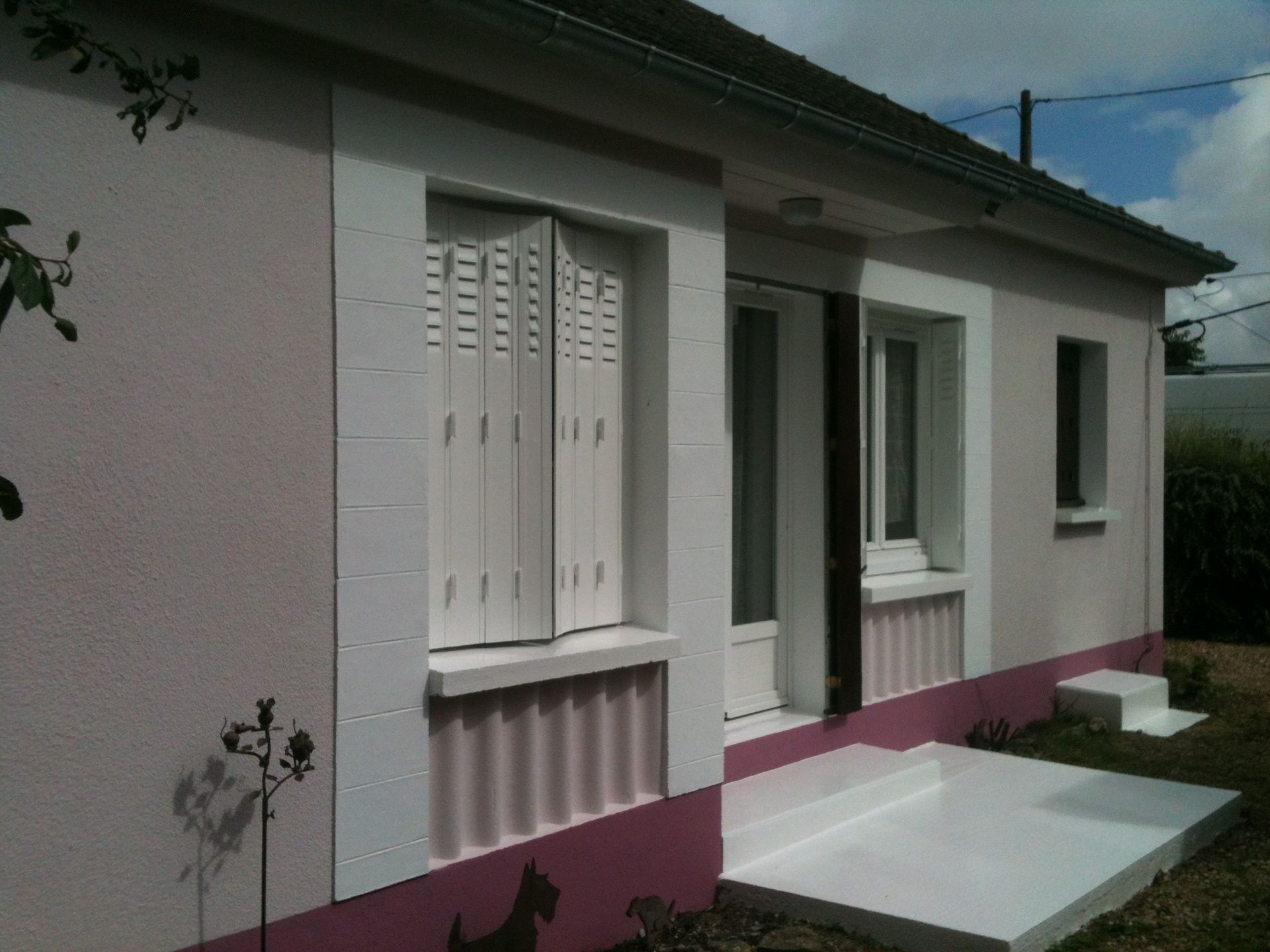 Photo d'une maison avec un crépi blanc et des bandes verticales roses en dessous des fenêtres