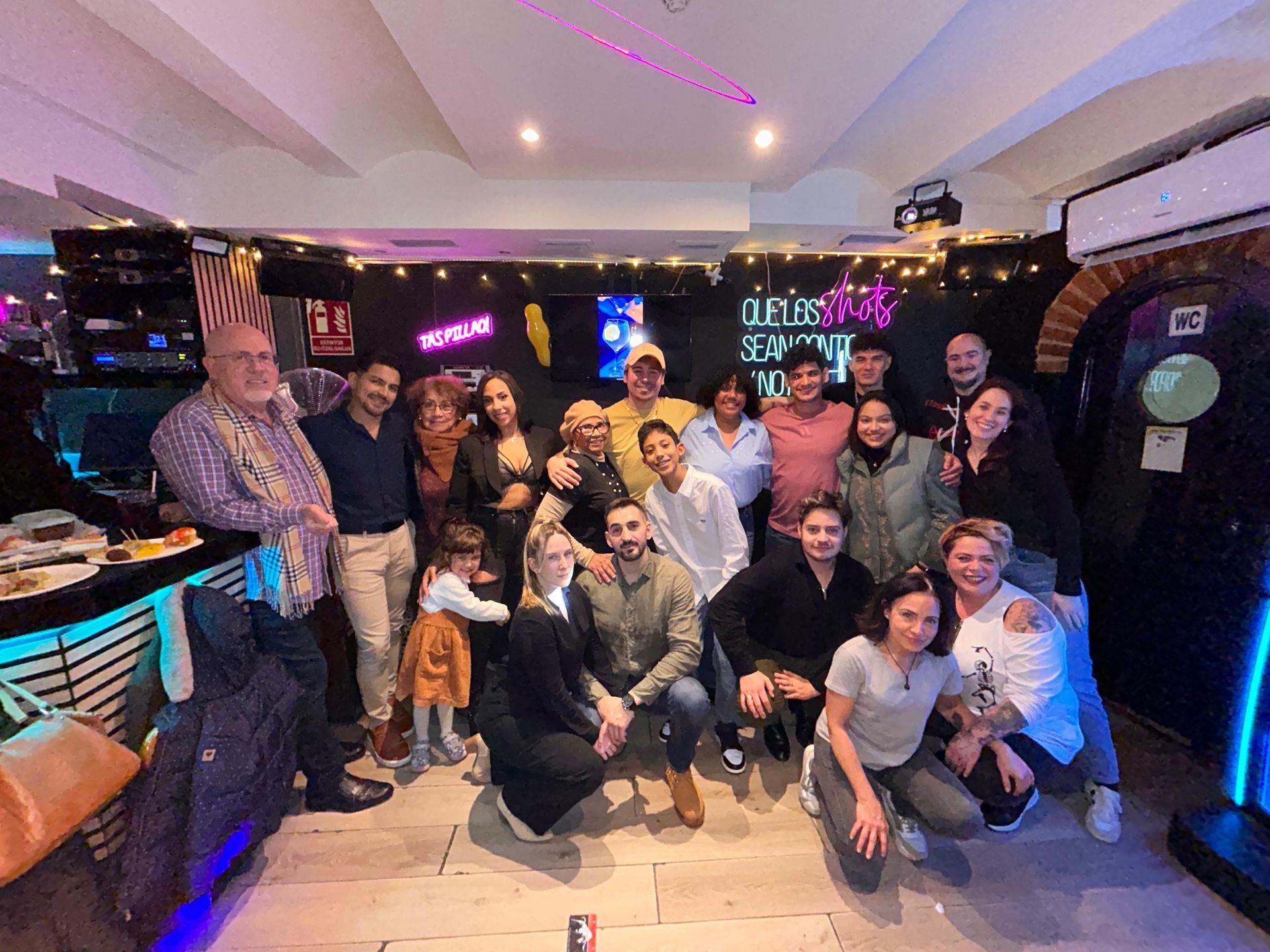 Un grupo de personas posando en un bar iluminado con luces de neón, sonriendo y agachándose juntas para una foto de grupo.