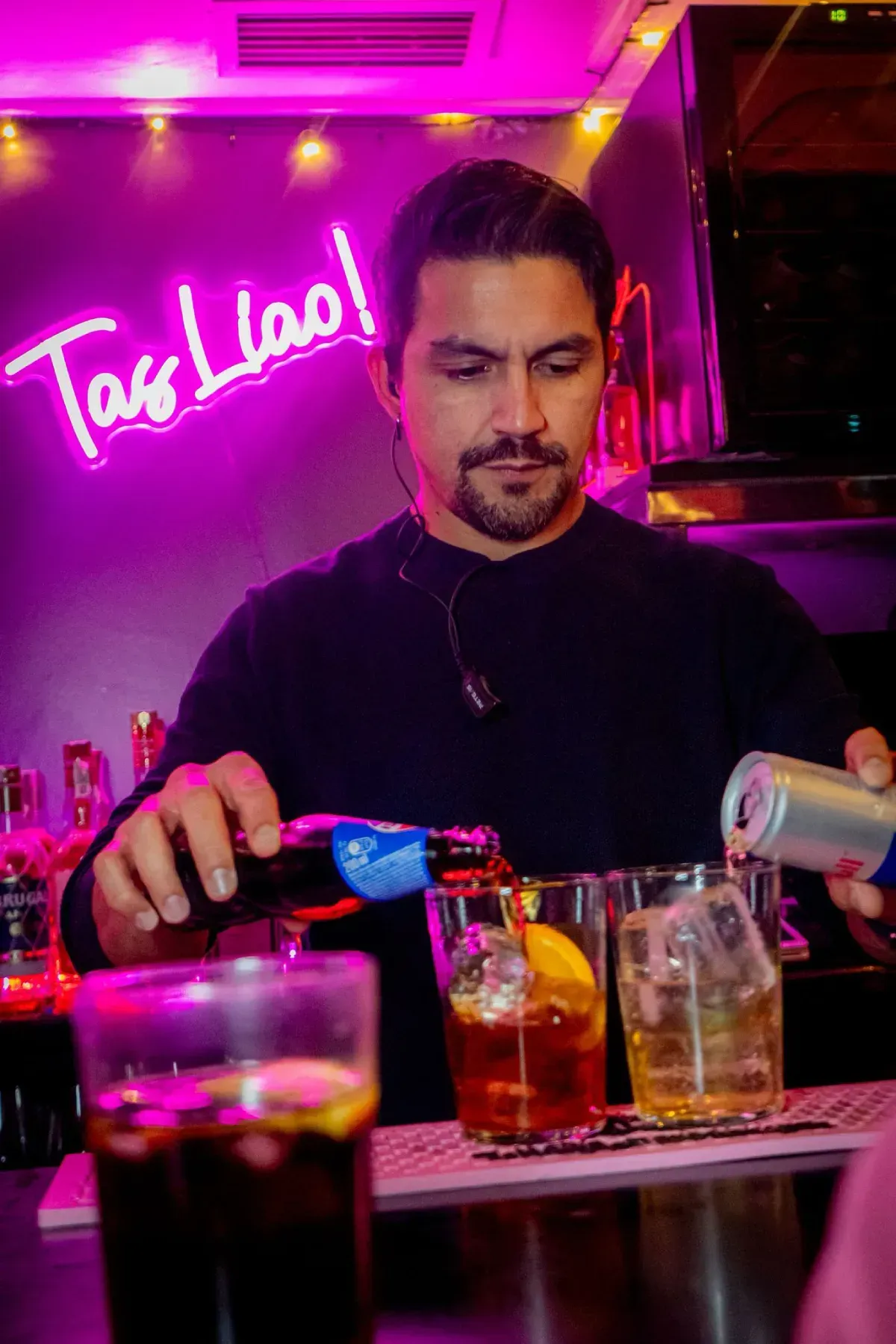 Camarero sirviendo bebidas detrás de una barra con un letrero de neón 