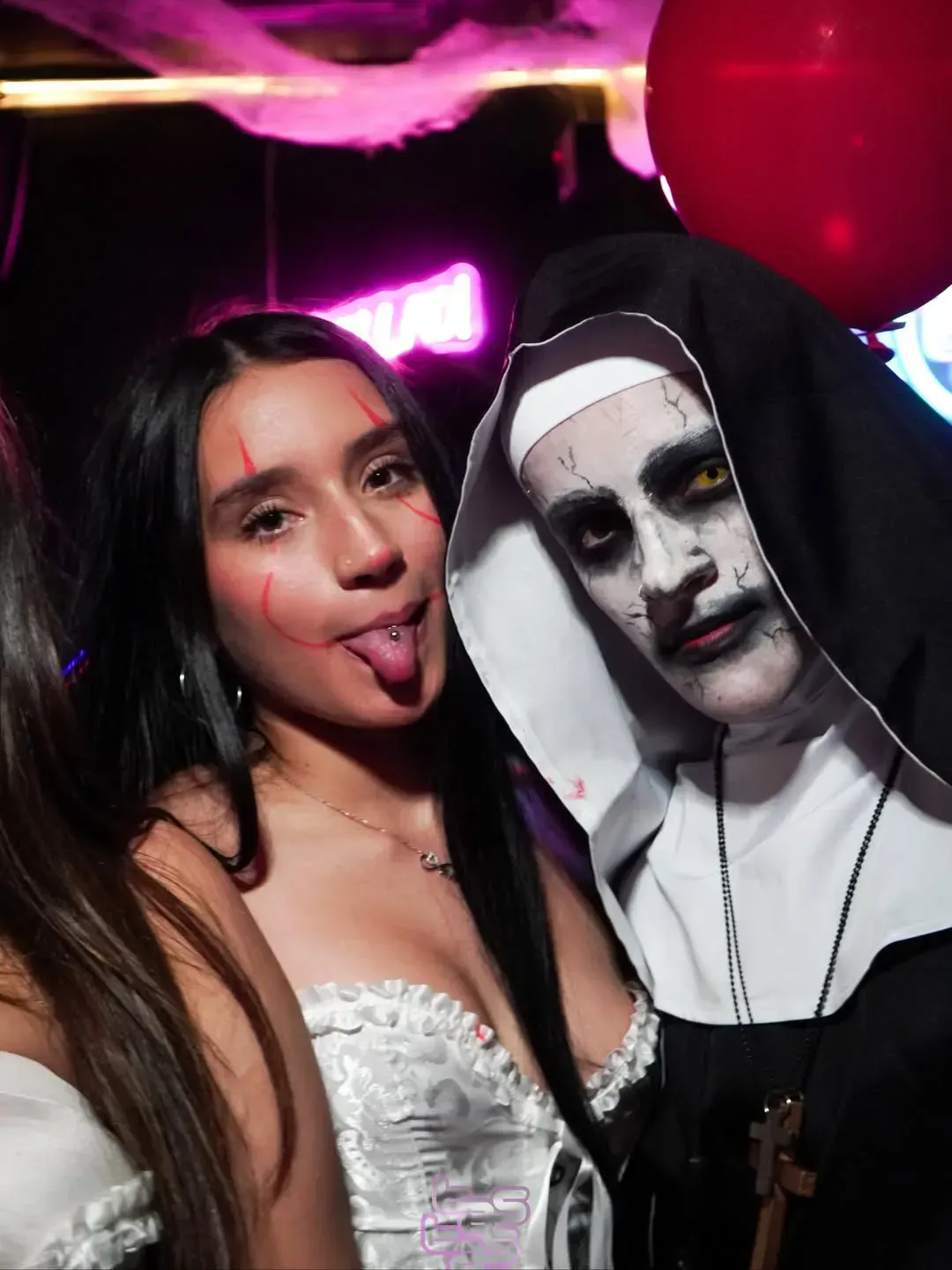 Mujer con vestido blanco y monja disfrazada posando con decoración de Halloween.