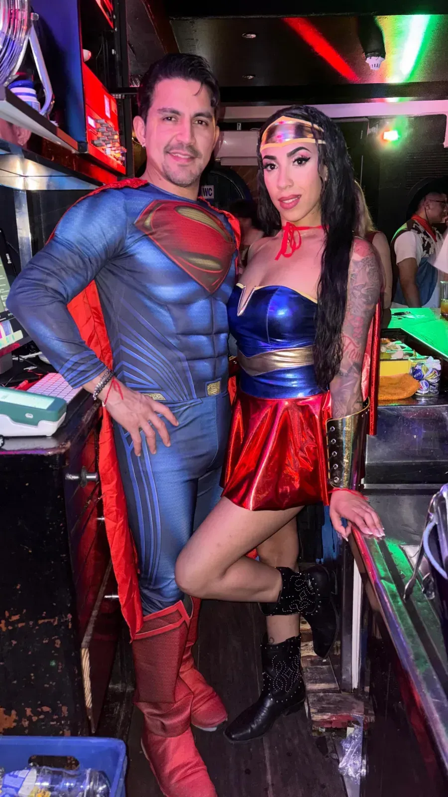 Un hombre disfrazado de Superman y una mujer disfrazada de Mujer Maravilla posan juntos en un evento.