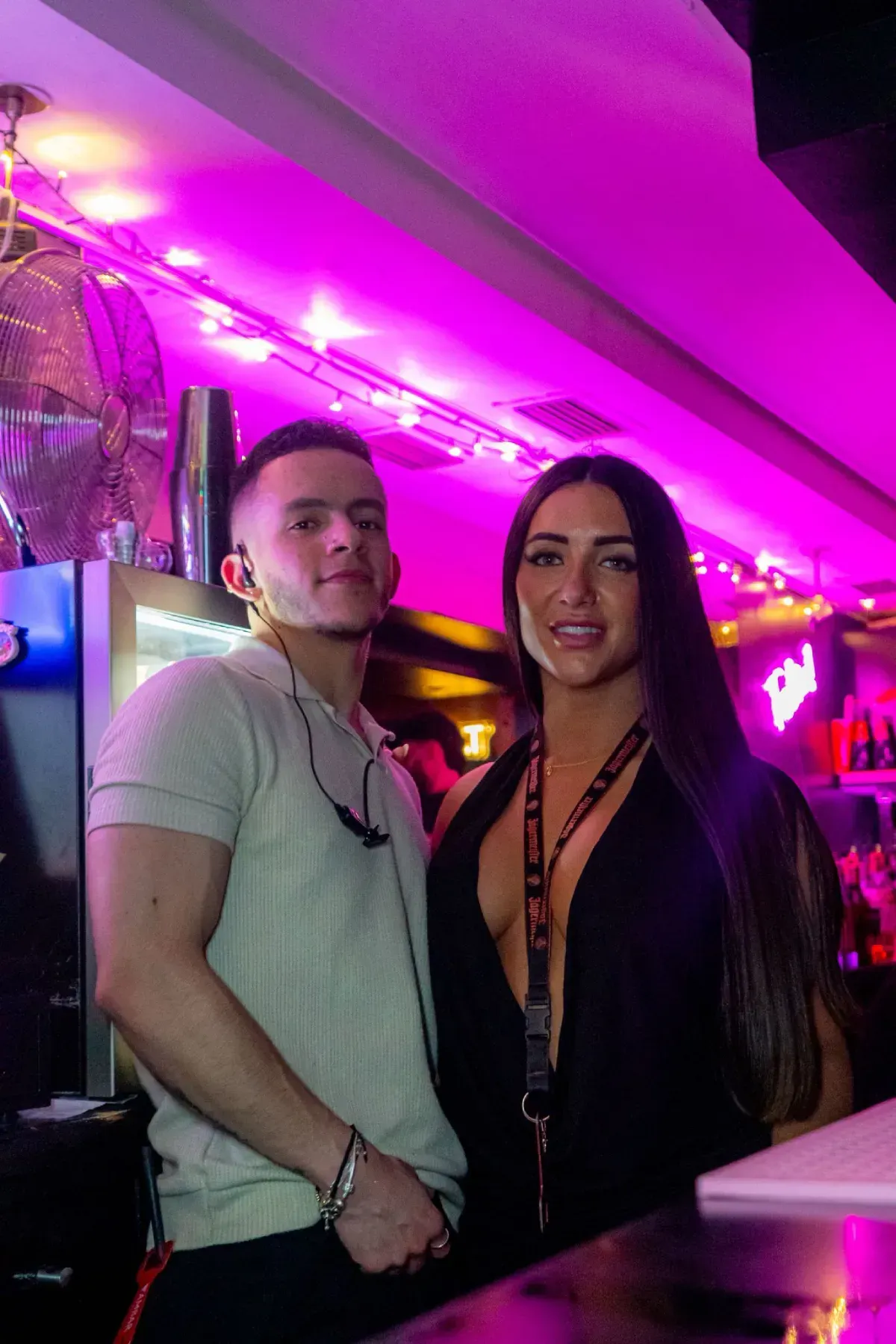 Hombre y mujer de pie juntos en un bar con iluminación rosa.