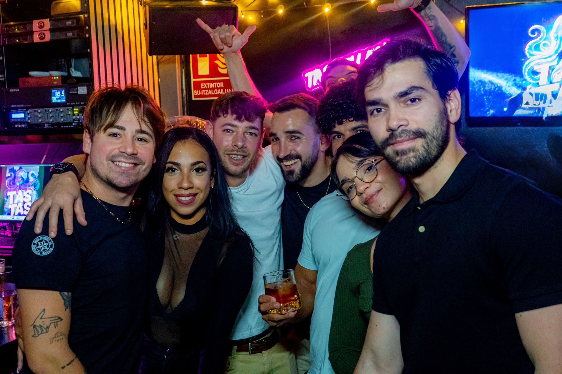 Grupo de personas sonriendo en un bar. Algunos se abrazan. Ambiente festivo con luces de colores.