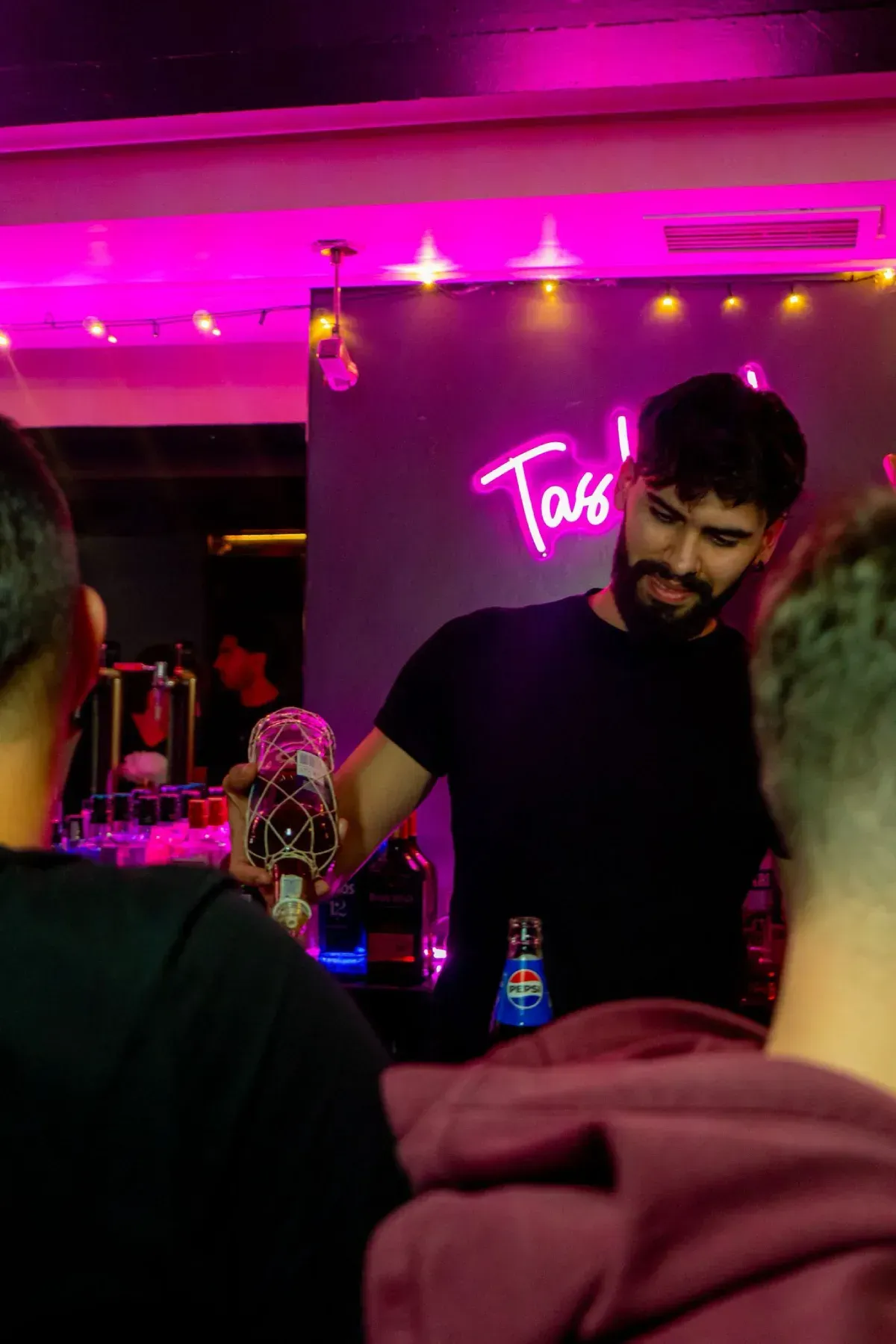 Camarero sirviendo una bebida en un bar con un letrero de neón rosa.