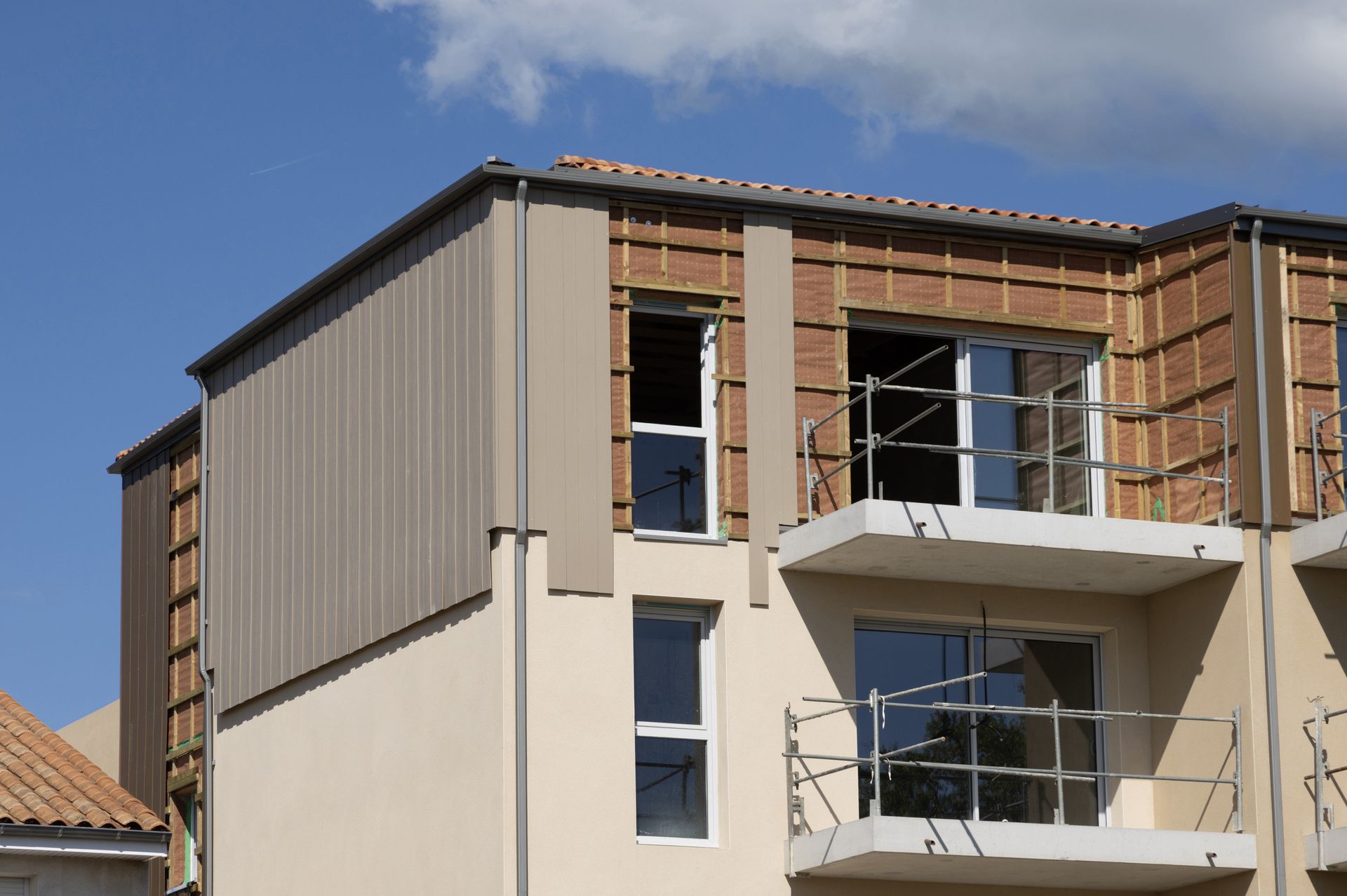 Façade d'un immeuble d'appartements moderne avec bardage beige, balcons et charpente apparente sous un ciel bleu