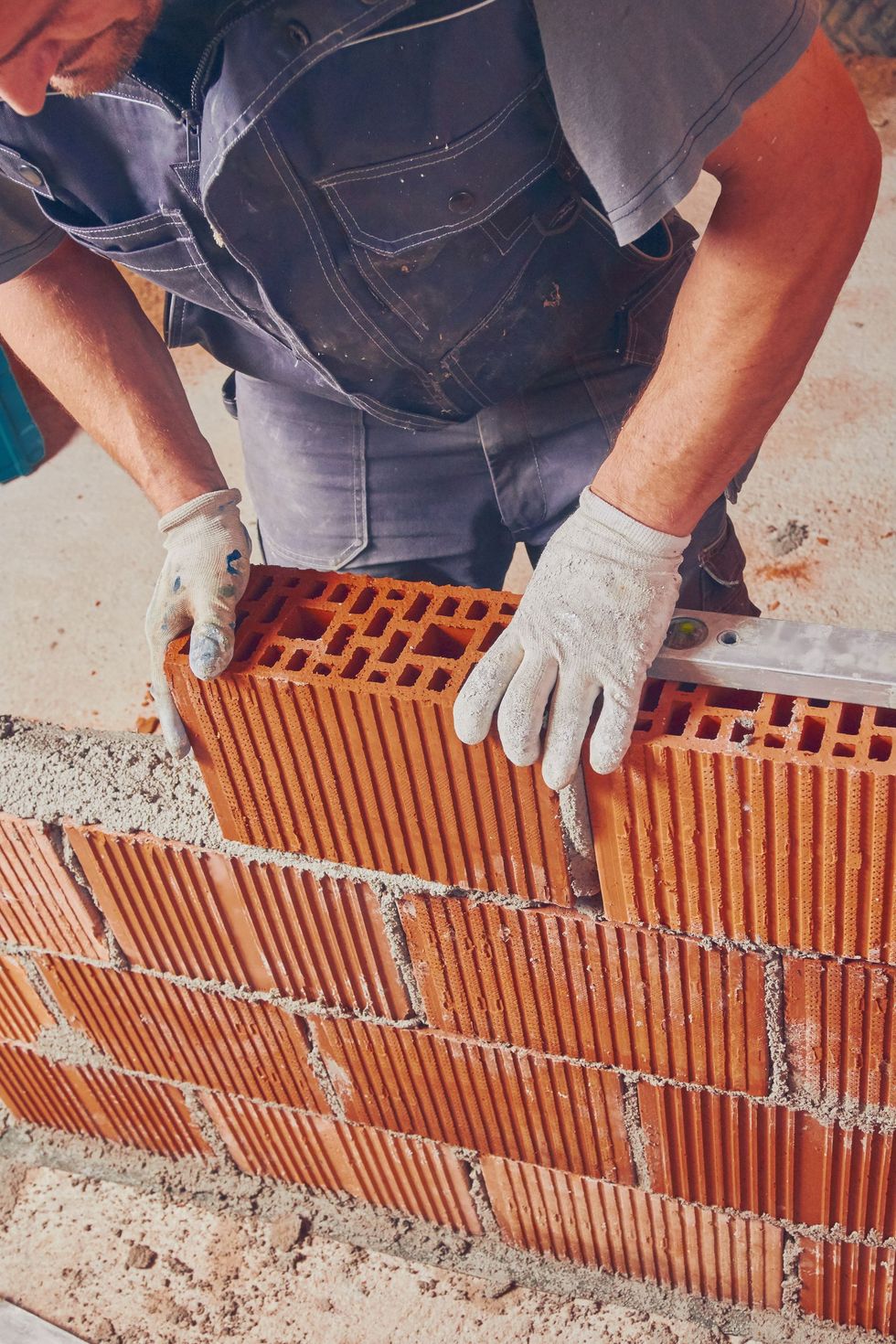 Ouvrier du bâtiment alignant des briques d'argile rouge avec des gants