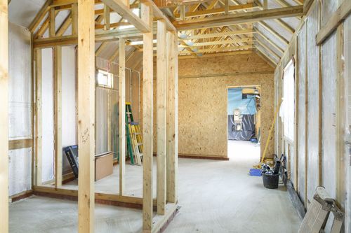Intérieur d'une maison en construction avec charpente en bois apparente et cloisons sèches non finies.