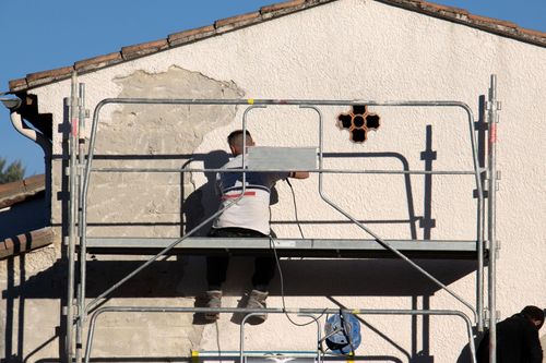 Ouvrier sur un échafaudage peignant au rouleau le mur extérieur d'une maison