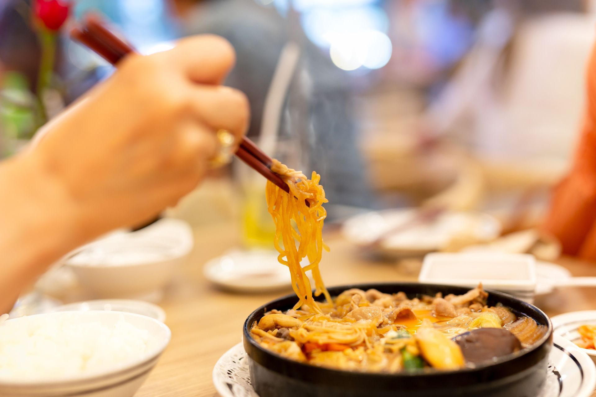 Una persona está comiendo fideos con palillos de un tazón de comida.