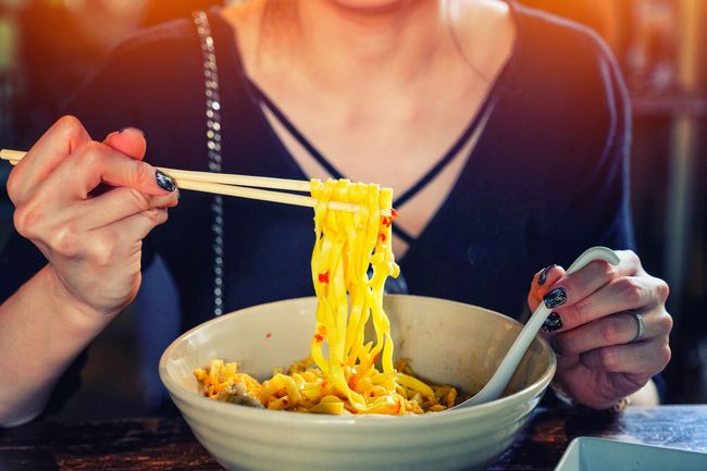 Una mujer está comiendo fideos con palillos de un tazón.