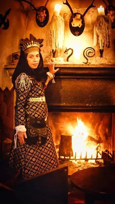 Una mujer con un vestido medieval está parada frente a una chimenea.