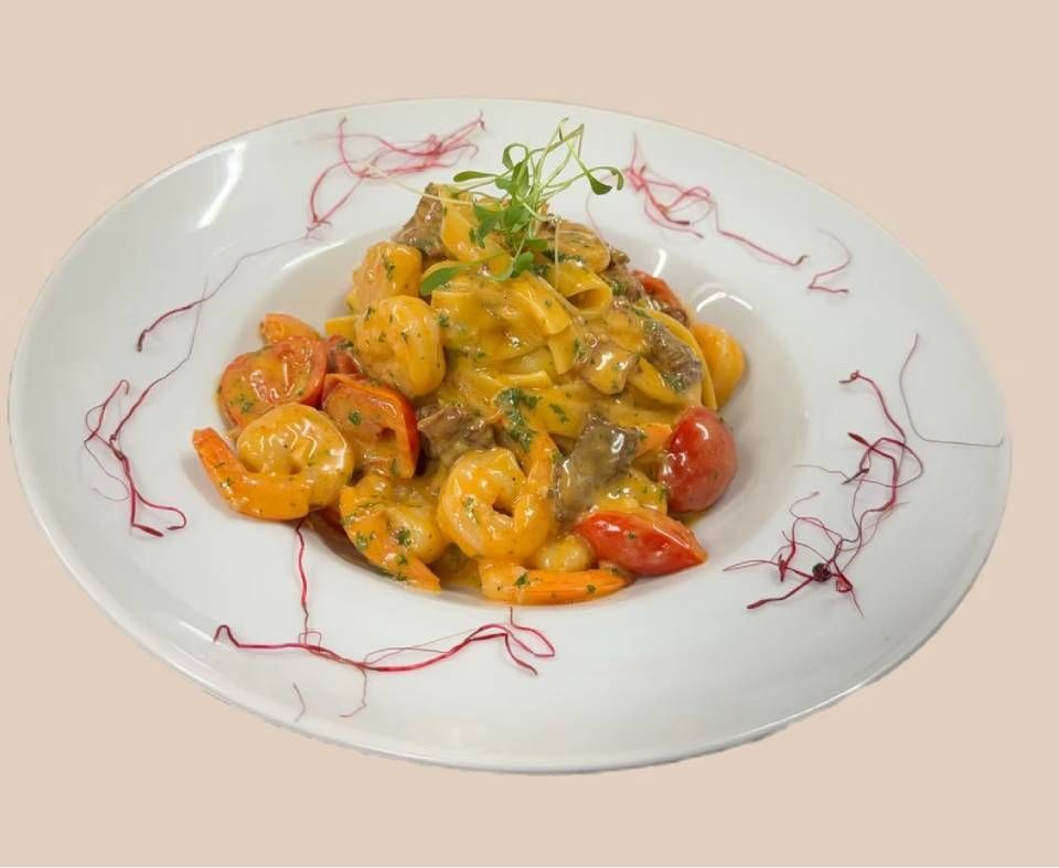 Plat de pâtes aux crevettes, tomates et champignons dans une sauce crémeuse, servi sur une assiette blanche.