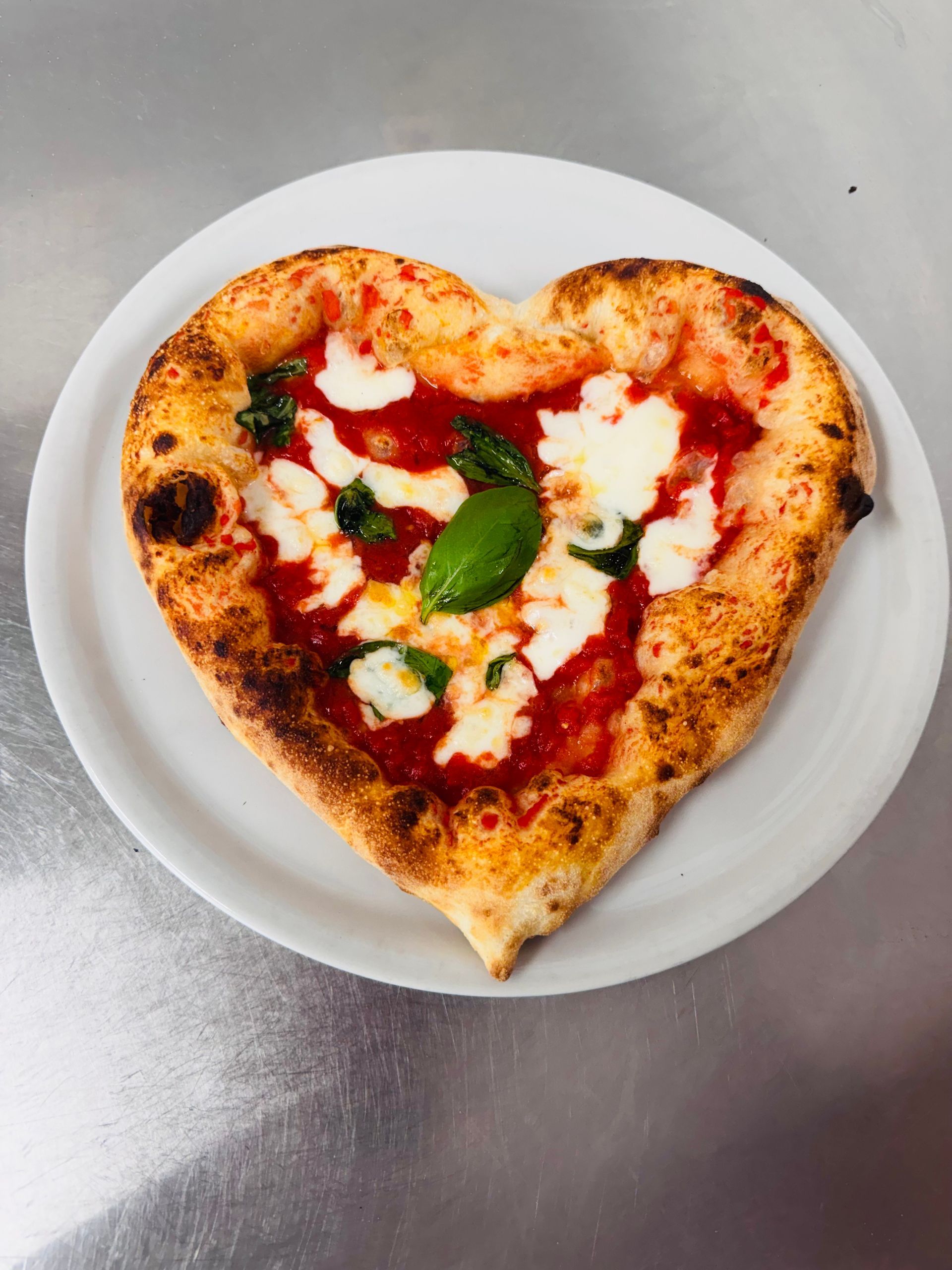 Un chef tient une pizza devant un four à bois. L'uniforme de Naples, un sourire amical et un four « VESUVIO ».