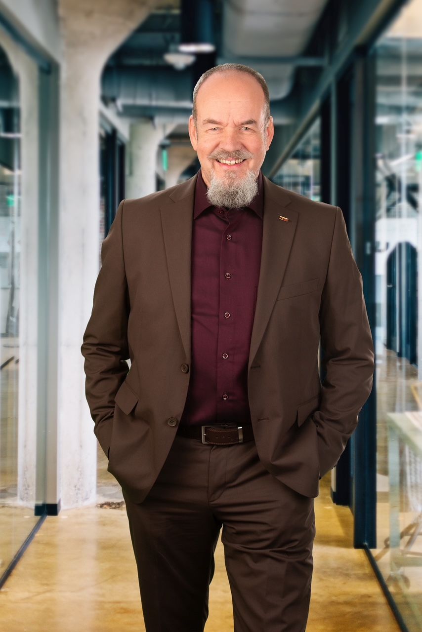 Ein Mann mit Bart und Schnurrbart lächelt auf einem Schwarzweißfoto.