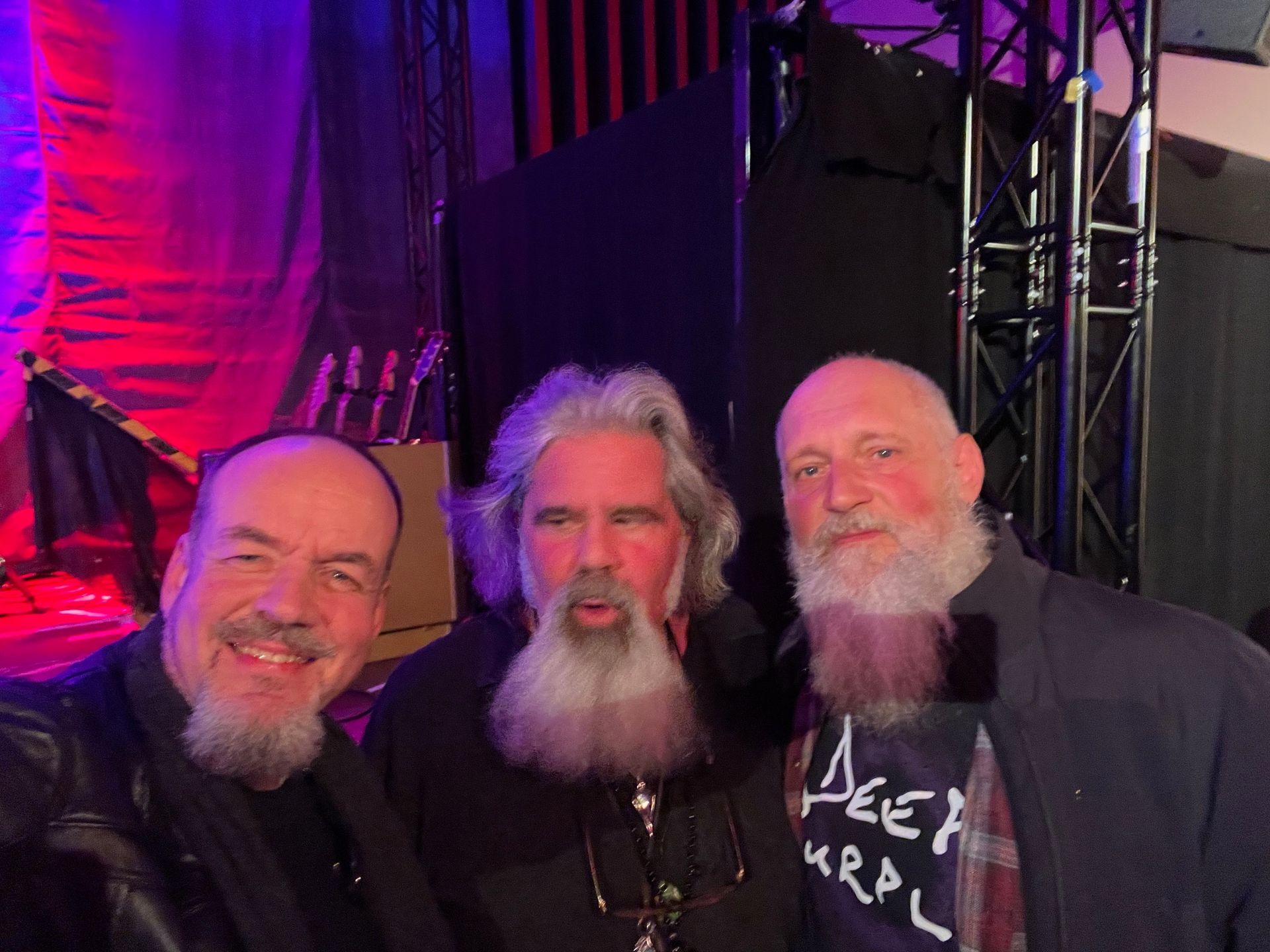 Drei Männer mit Bärten stehen zusammen in einem Konzertsaal, einer von ihnen trägt ein Deep Purple-Shirt.