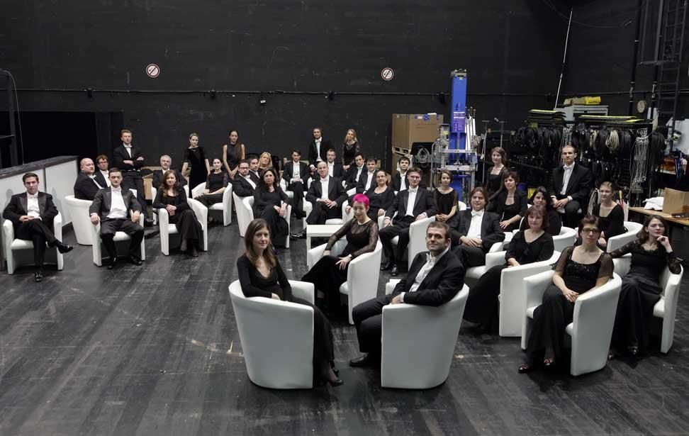 Eine große Gruppe von Menschen sitzt auf Stühlen in einem dunklen Raum