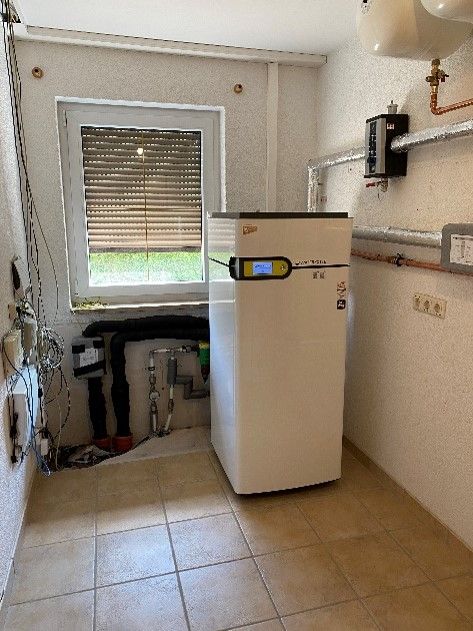 Ein weißer Kühlschrank steht in einem Raum neben einem Fenster.