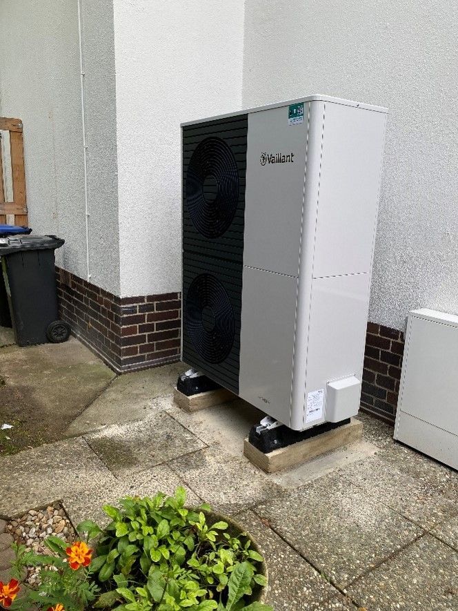 Eine große weiß-schwarze Klimaanlage steht auf einer Terrasse neben einer Backsteinmauer.