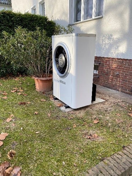 Eine weiße Waschmaschine steht im Gras vor einem Haus.
